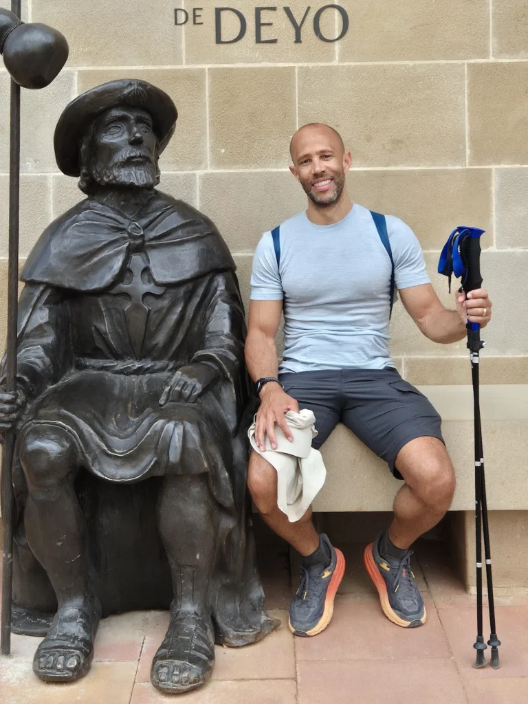 Simon sitting next to a bronze statue on the Camino de Santiago