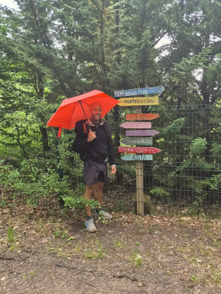 Simon under an orange umbrella standing next to place signs in a forest
