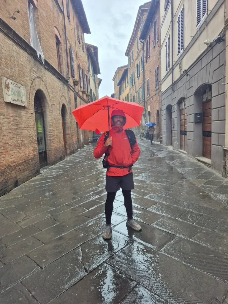 Simon standing with an umbrella on a wet cobbled street in Siena