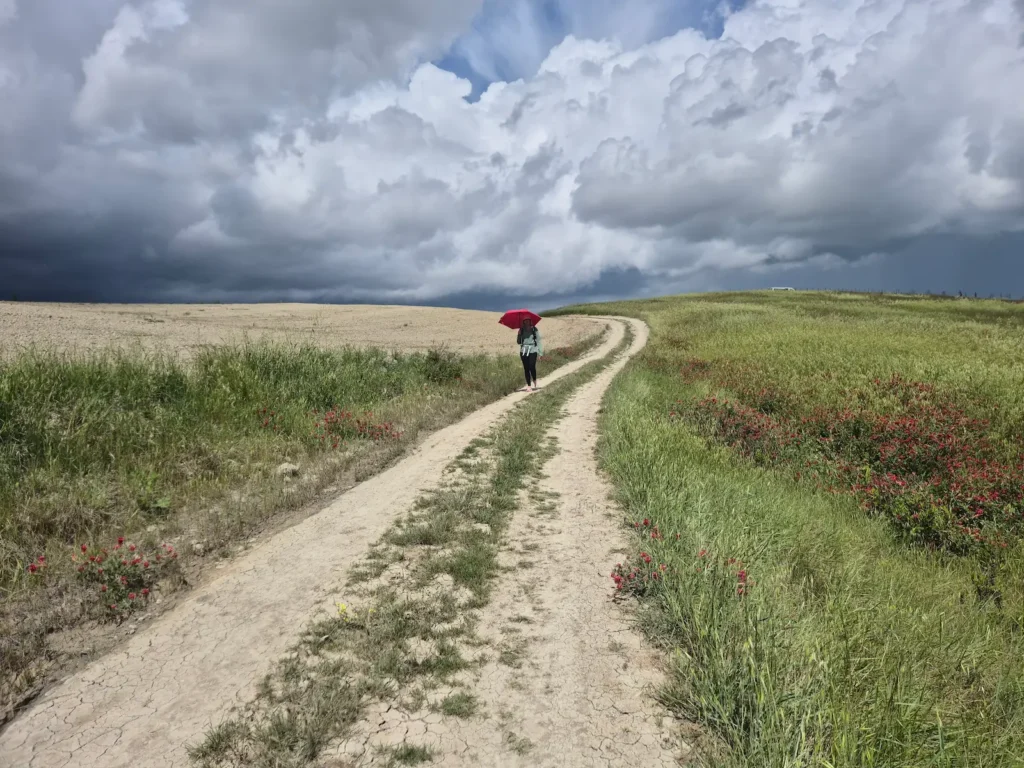 Eve with a red umbrella walking along a gravel track, with dark grey skies behind her