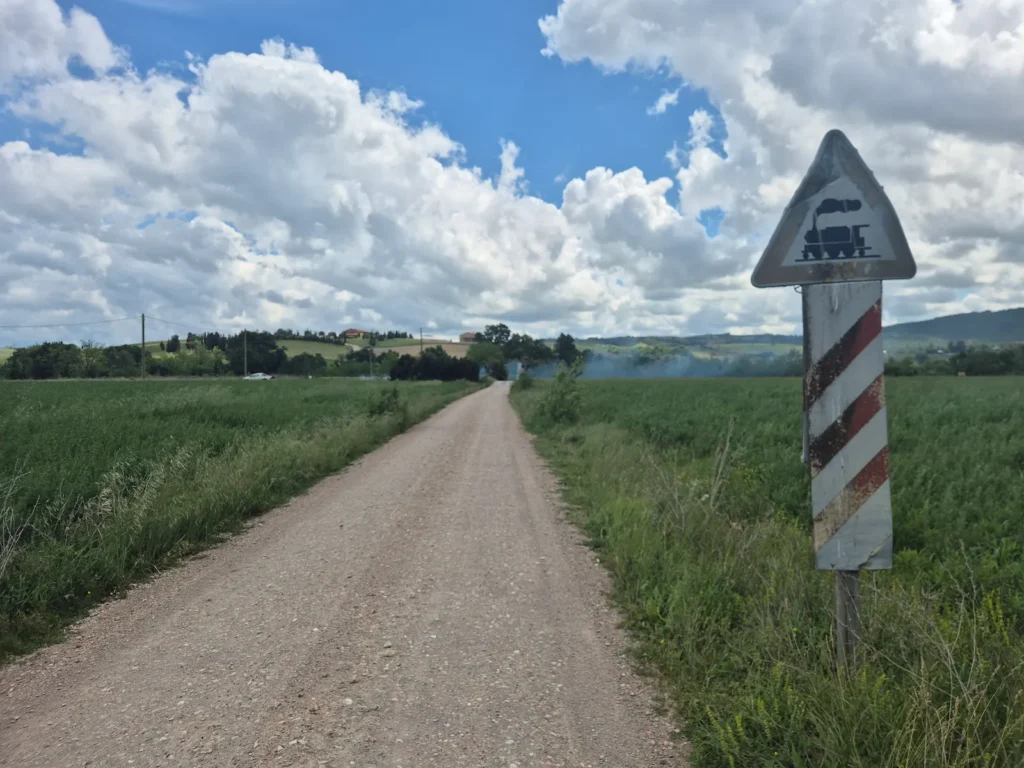 Gravel track through a wheat field with a train crossing sign on the side