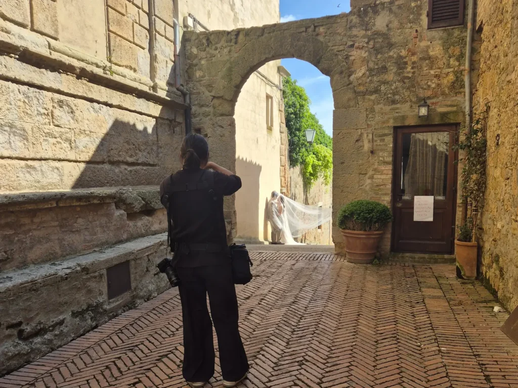 Photographer taking a photo through a medieval arch of a wedding couple in Pienza