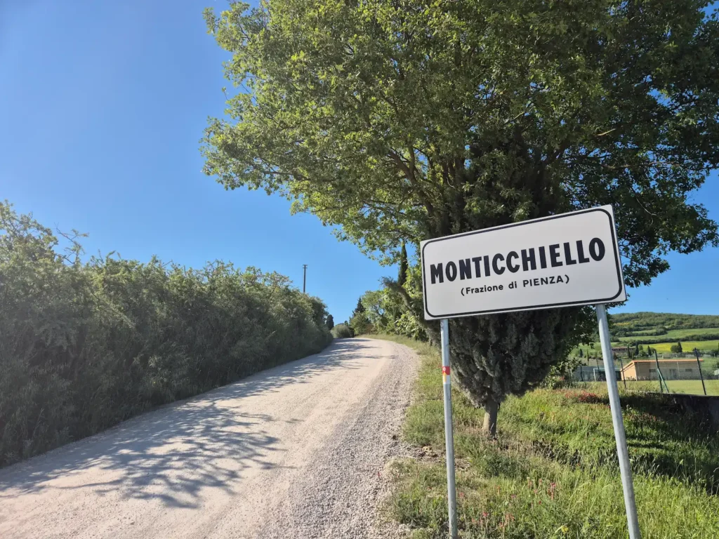 A gravel road with a Monticchiello sign on the side